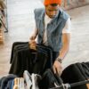 Man examines clothing in boutique wearing denim vest and orange beanie.