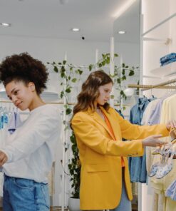 Two women shopping in a trendy clothing store, browsing stylish outfits.